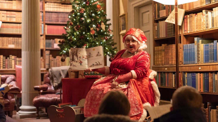 Mrs Christmas sitting in a library holding a book and reading a story in Wallington, Northumberland